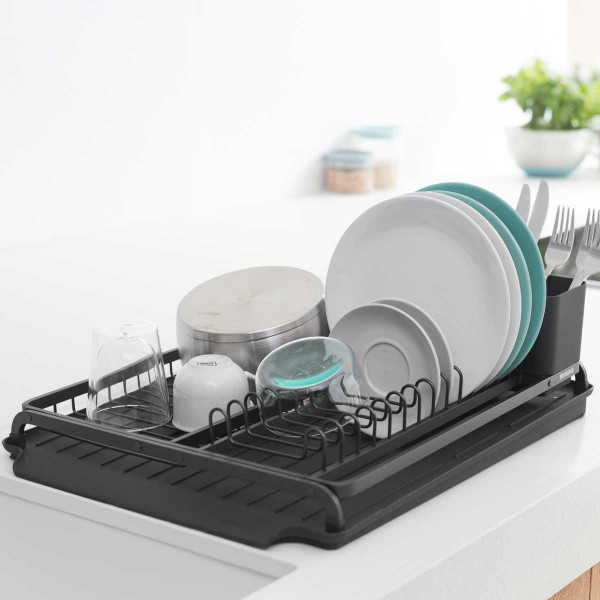 התקן ייבוש כלים גדול שחור Brabantia יושב על משטח לבן, מחזיק בצורה מסודרת צלחות, קערות, כוסות, כלים ומיכל. ירק וצנצנות מטבח מספקות תוספת סטיילינג והום דקור ברקע הפוקוס הרך. - vavaVoom.co.il