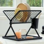 התקן ייבוש כלים מתקפל קטן שחור Brabantia מוסיף סטיילינג לדלפק המטבח שלך, מחזיק צלחות, כוסות וכלים. ליד החלון עם נוף ירוק, הוא מביא קסם של כלי בית לדלפקים ומסגרות לבנים פריכים. - vavaVoom.co.il