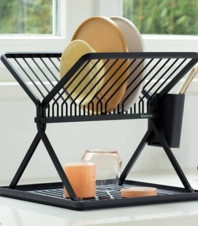 התקן ייבוש כלים מתקפל קטן שחור Brabantia מוסיף סטיילינג לדלפק המטבח שלך, מחזיק צלחות, כוסות וכלים. ליד החלון עם נוף ירוק, הוא מביא קסם של כלי בית לדלפקים ומסגרות לבנים פריכים. - vavaVoom.co.il