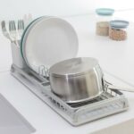 התקן ייבוש כלים קטן אפור Brabantia על השיש מחזיק סיר, שתי צלחות וסכו"ם, כשברקע שני צנצנות עם קטניות מוסיפות לקטע דקור נקי וסטיילינג מינימליסטי לכלי בית. - vavaVoom.co.il