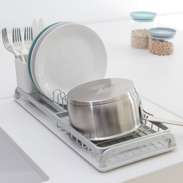התקן ייבוש כלים קטן אפור Brabantia על השיש מחזיק סיר, שתי צלחות וסכו"ם, כשברקע שני צנצנות עם קטניות מוסיפות לקטע דקור נקי וסטיילינג מינימליסטי לכלי בית. - vavaVoom.co.il