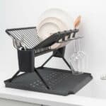מתקן ייבוש כלים מתקפל גדול שחור Brabantia מחזיק צלחות, קערות, סכו"ם ושתי כוסות יין הפוכות. המתקן מונח על מגש ניקוז עם פסי גומי ליד כיור לבן ומוסיף הום דקור וסטיילינג למטבח. - vavaVoom.co.il
