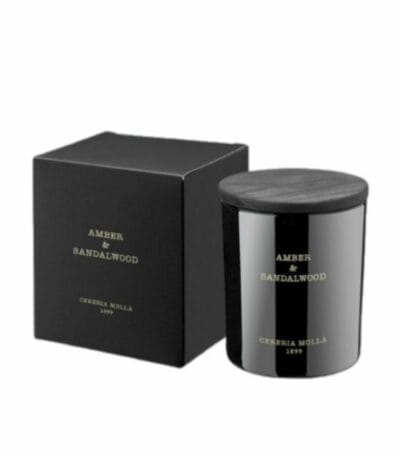 צנצנת נרות שחורה עם הכיתוב "נר קטן AMBER&SANDALWOOD - גר׳ 230" מונחת לצד הקופסה השחורה התואמת, ששתיהן מעוטרות בכיתוב זהוב פשוט על רקע לבן חלק. - vavaVoom.co.il